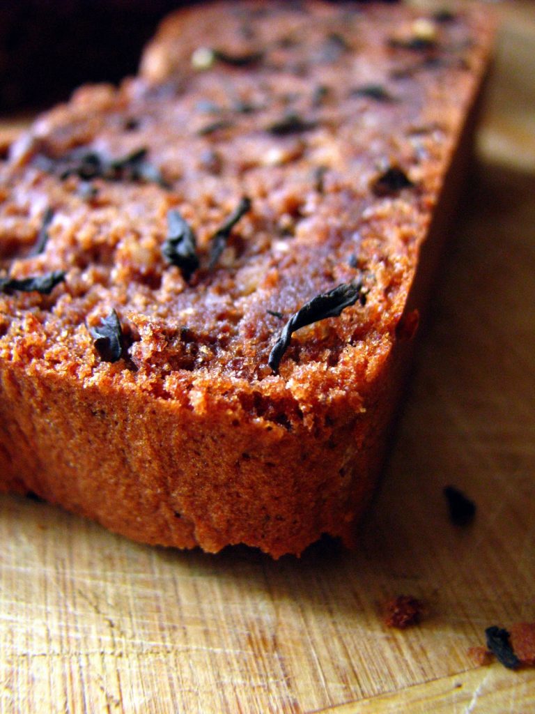 Tranche de cake au chocolat aromatisé au thé avec quelques feuilles de thé en décoration sur le dessus.