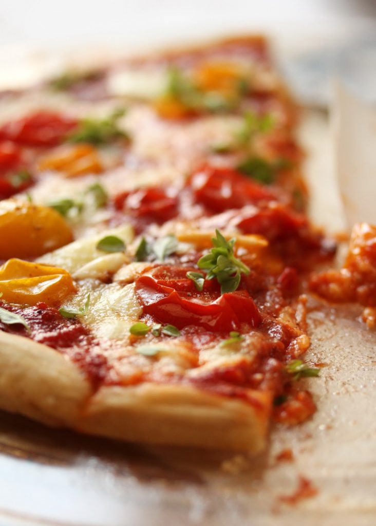 Part de pizza maison Margarita au coulis de tomates, tomates fraîches, basilic et mozzarella posée sur une plateau en bois