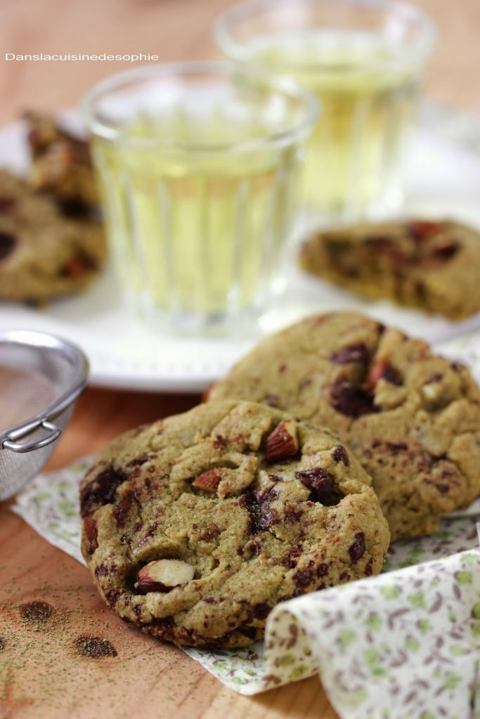 Cookies vegan aux amandes, matcha et chocolat posés sur un tissu fleuri. A l'arrière plan, deux verres de thé verts et quelques cookies posés sur une assiette blanche