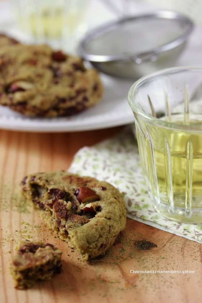 Gros plan sur un cookie - coupé en deux - au matcha amande et chocolat posé à côté d'un verre de thé vert