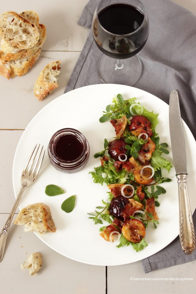 Assiette vue de haut contenant une salade de mesclun avec de la ventrèche grillée, des prunes poêlées au miel de vin rouge et des oignons. 