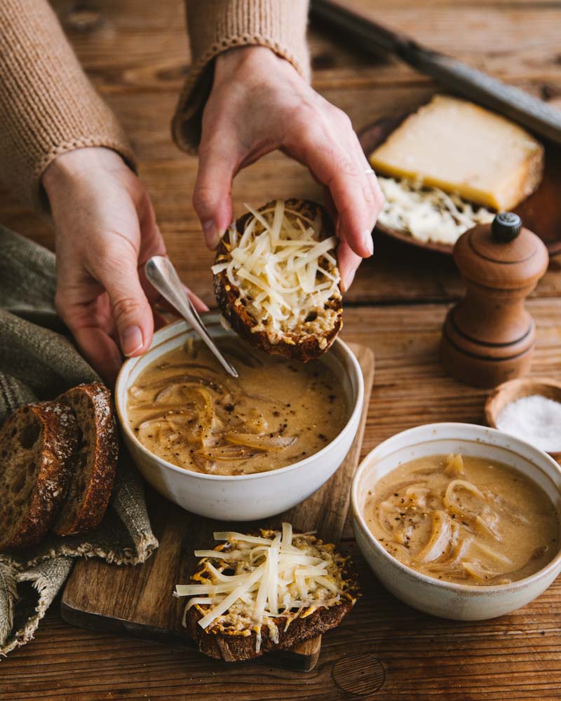 Mains tenant un bol de soupe à l'oignon et une tartine de pain au fromage gratiné