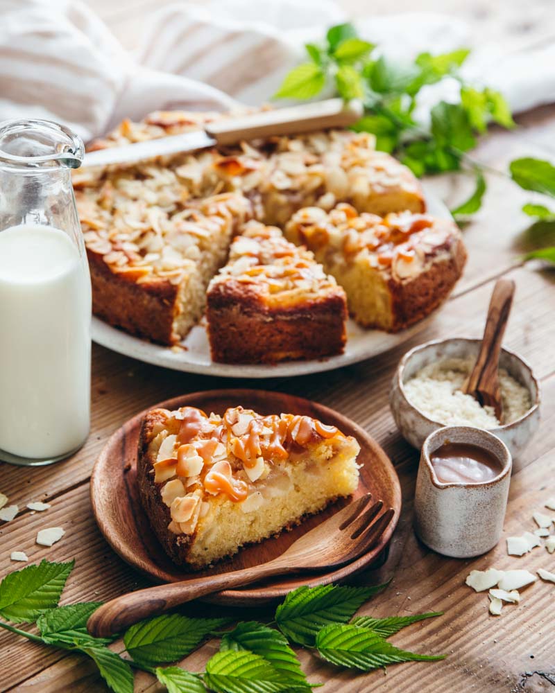 Gâteau au yaourt, poires et amandes posé sur assiette et découpé sur une table en bois. Servi avec du caramel au beurre salé. 