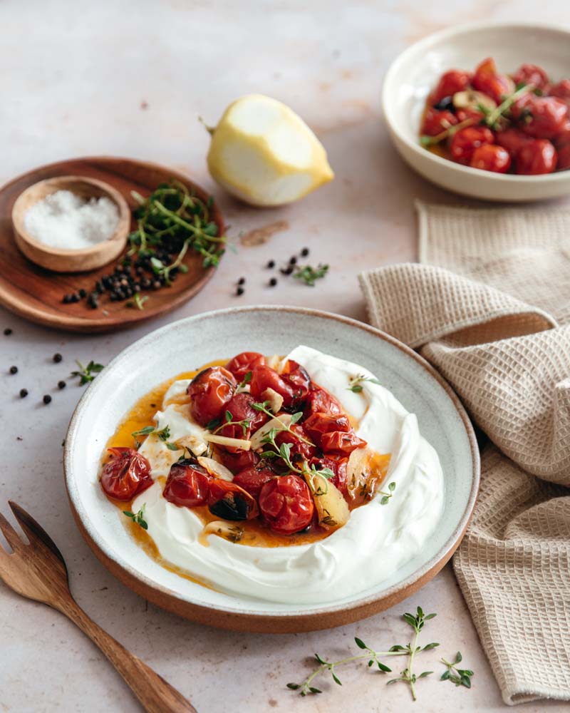 Assiette présentant des tomates cerises cuites au four avec des herbes fraîches, du citron et des épices servies avec du yaourt à la grecque. 
