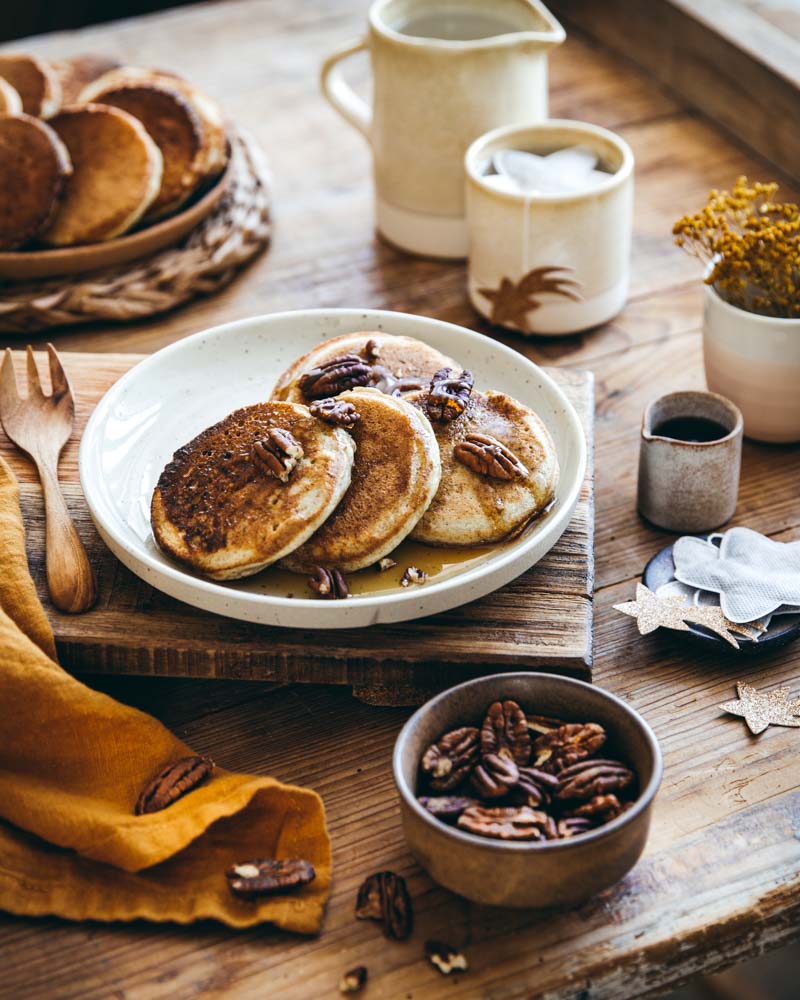 Assiette en grès contenant des pancakes au levain maison, servis avec du sirop d'érable et des noix de pécan. Ambiance goûter. 