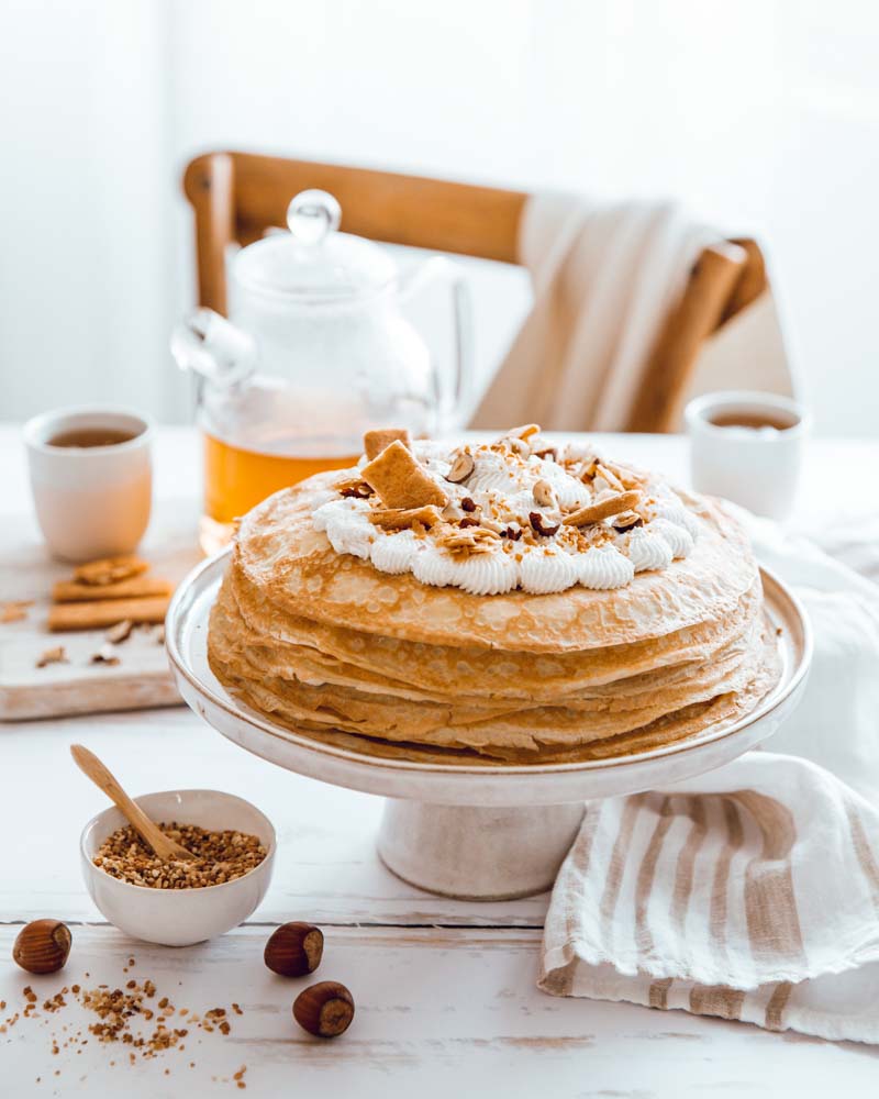 Gâteau de crêpes à la pâte à tartiner et chantilly maison, décoré de noisettes, pralin et biscuits crêpes dentelle dans une ambiance teatime dans lestons blancs. 