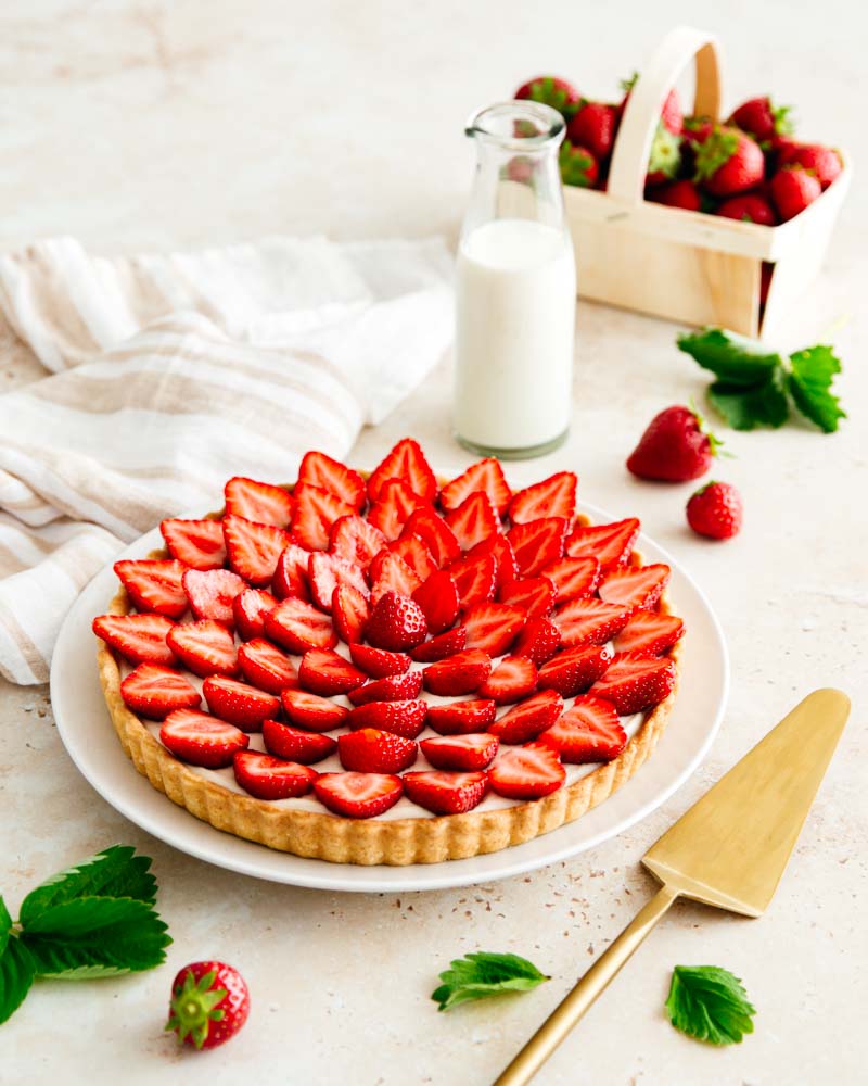 Tarte aux fraises composée d'une pâte sablée, d'une crème diplomate et de fraises fraîches coupées en deux dans une ambiance minimaliste. 