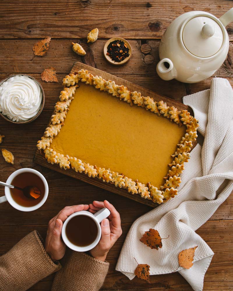 Tarte pumpkin pie à l'heure du goûter avec deux tasses de thé et de la crème fouettée dans une ambiance chaleureuse et automnale. 