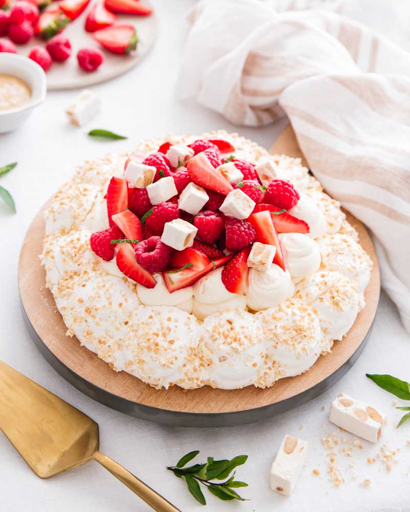 Pavlovu aux éclats de nougat et à la chantilly au nougat garnie de fraises et de framboises. Un dessert parfait pour un anniversaire ou la fête des mères. 