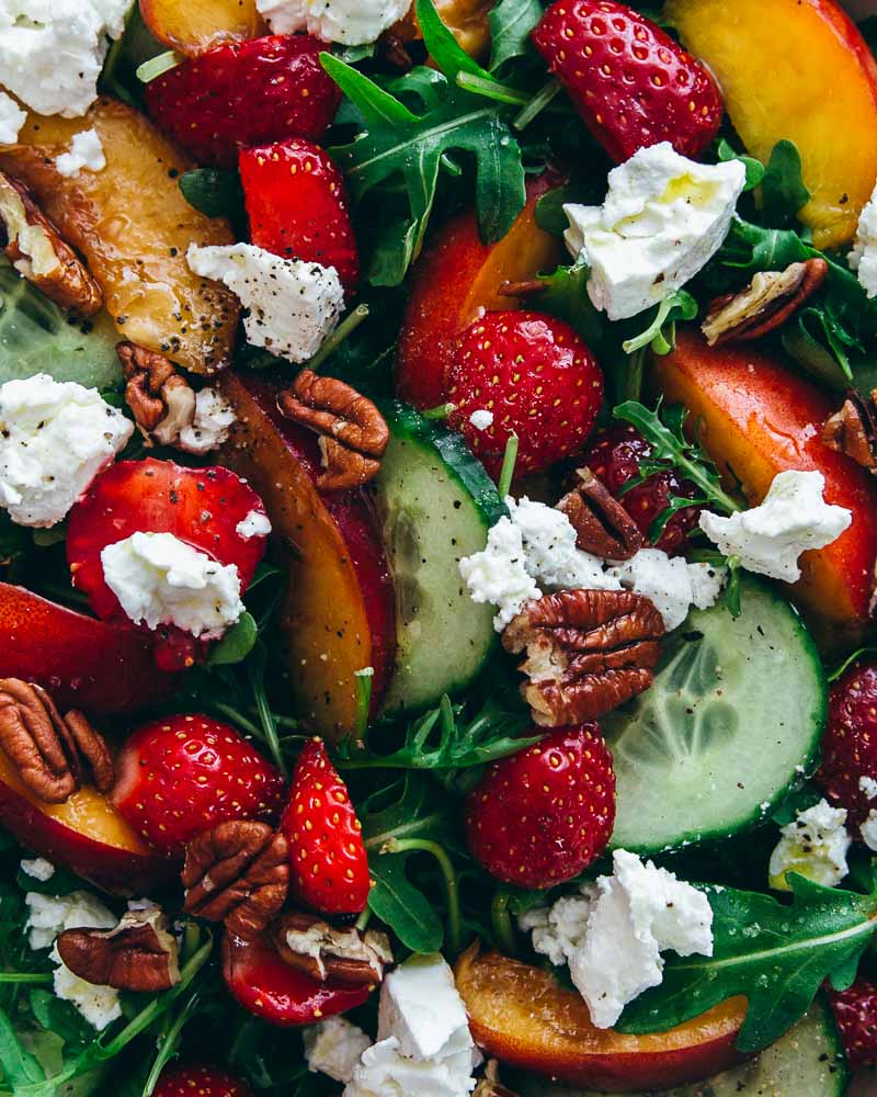 Détail en gros-plan d'une salade composée de nectarine, fraise, concombre, salade de roquette, chèvre frais et noix de pécan avec un peu d'huile d'olive. 