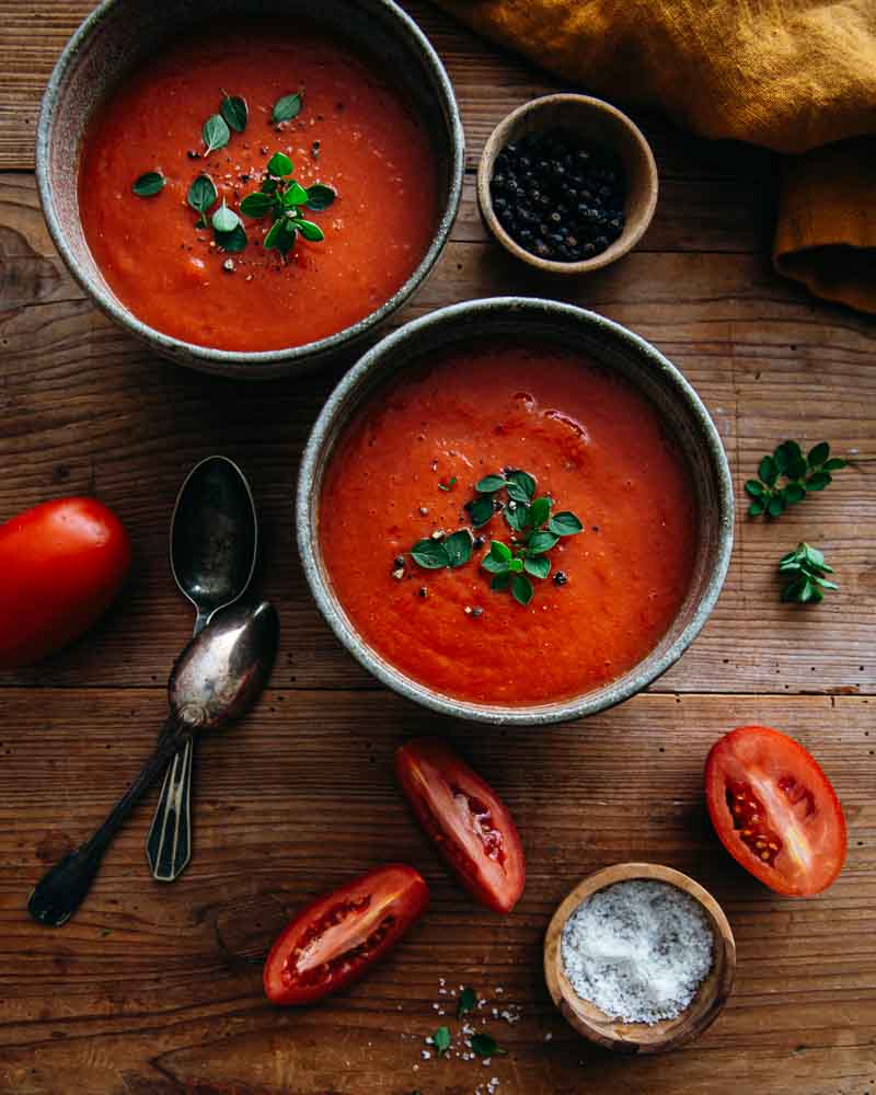 Gros plan sur deux bols en céramique garnis de soupe e tomates avec des feuilles d'origan frais et du poivre concassé. 
