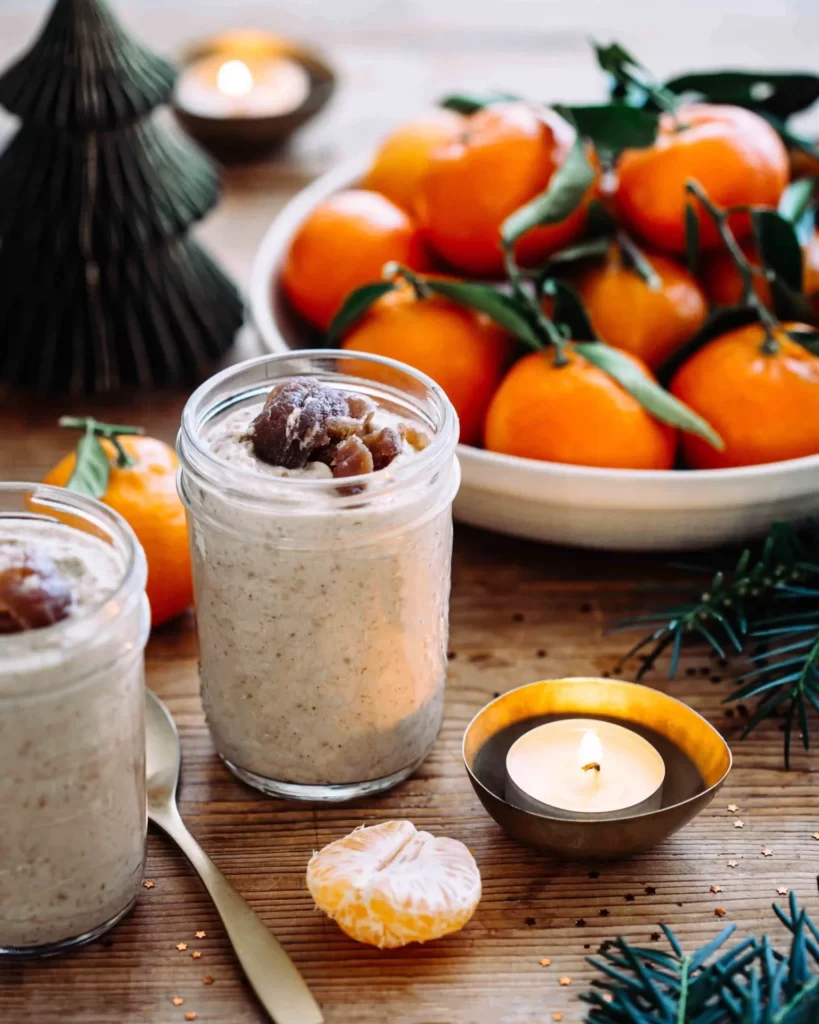 Focus sur un pot de mousse de marrons aux pommes avec des marrons glacés dans un décor rustique festif avec des branches de sapin et des clémentines. 