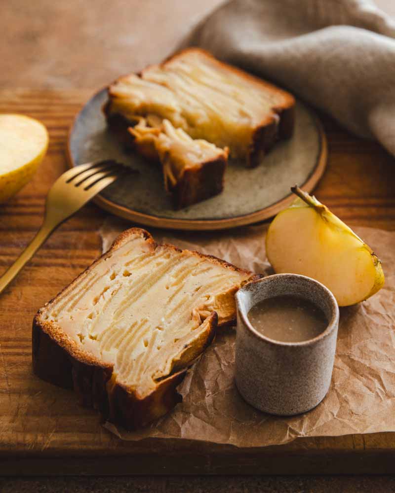 Tranches de gâteau invisible aux pommes. A côté un petit récipient à bec verseur avec du caramel au sirop d'érable et des quartiers de pomme Chanteclerc parfaites pour réaliser ce dessert.