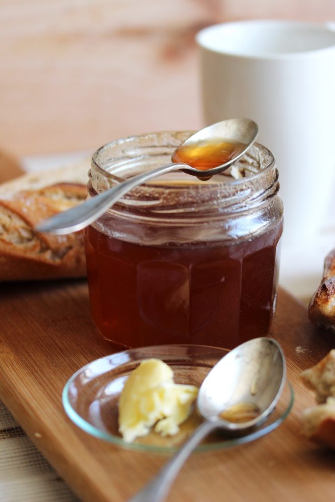 Pot de gelée de pommes au thé Earl Grey ouvert avec une cuillère présentant sa couleur dorée. 