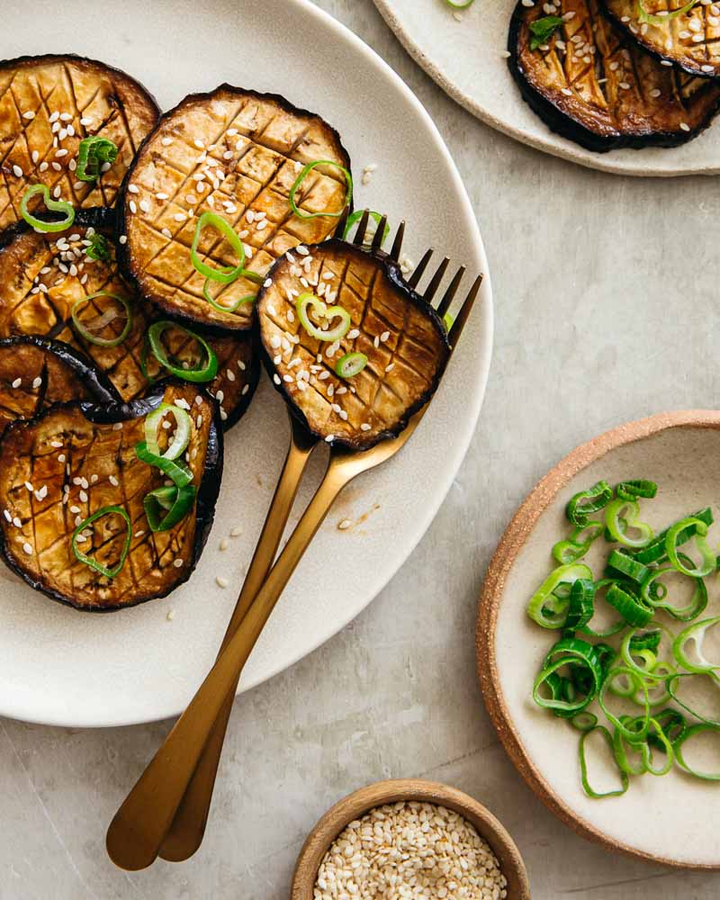 Assiette de tranches d'aubergines sauce miso servies avec de la cébette ciselée et des graines de sésame