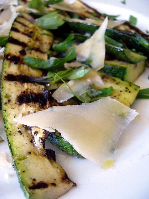 Lamelles de courgettes grillées servies avec des copeaux de parmesan, de l'huile d'olive et des feuilles de basilic