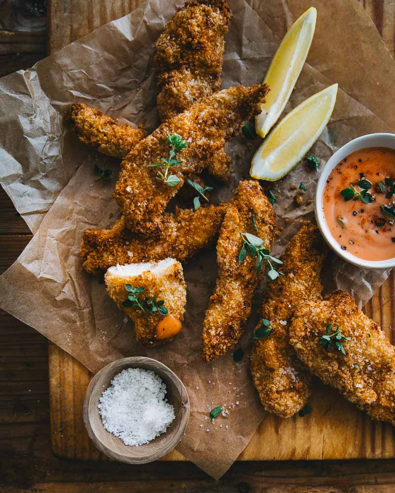 Planche d'aiguillettes de poulet panés cuisson Air Fryer servis avec des quartiers de citron et avec unesauce cocktail