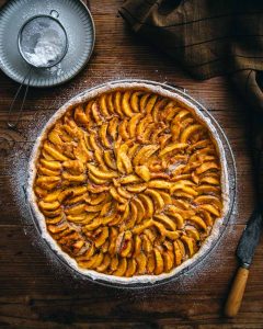 Tarte aux pêches démoulée prête à être dégustée avec un peu de sucre glace sur les bords de la pâte