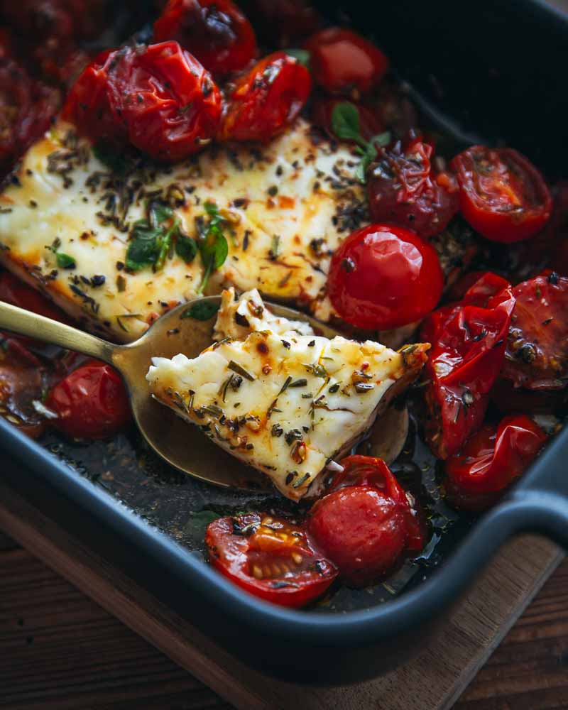 Cuillère avec un morceau de féta rôtie dedans. Autour des tomates rôties à l'Air Fryer.