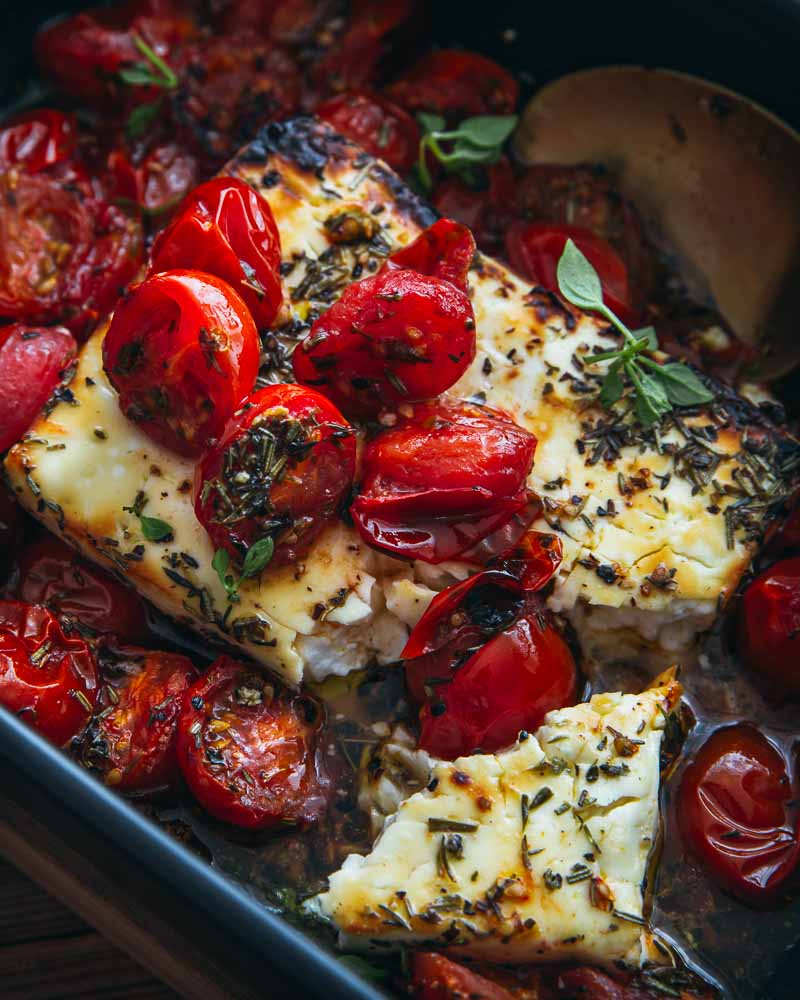 Gros plan sur des tomates cerise rôties et un bloc de féta avec des herbes de Provence. 