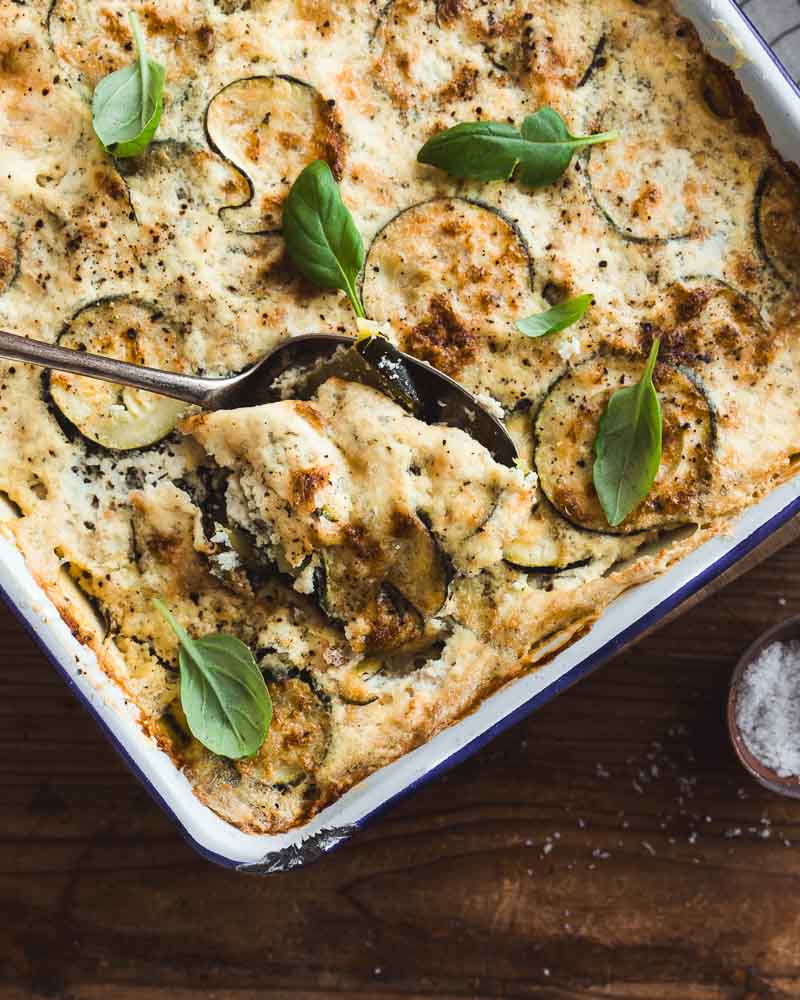 Vue de haut d'un gratin de courgettes vegan au tofu soyeux, à la crème de soja et purée d'amandes avec une cuillère dedans