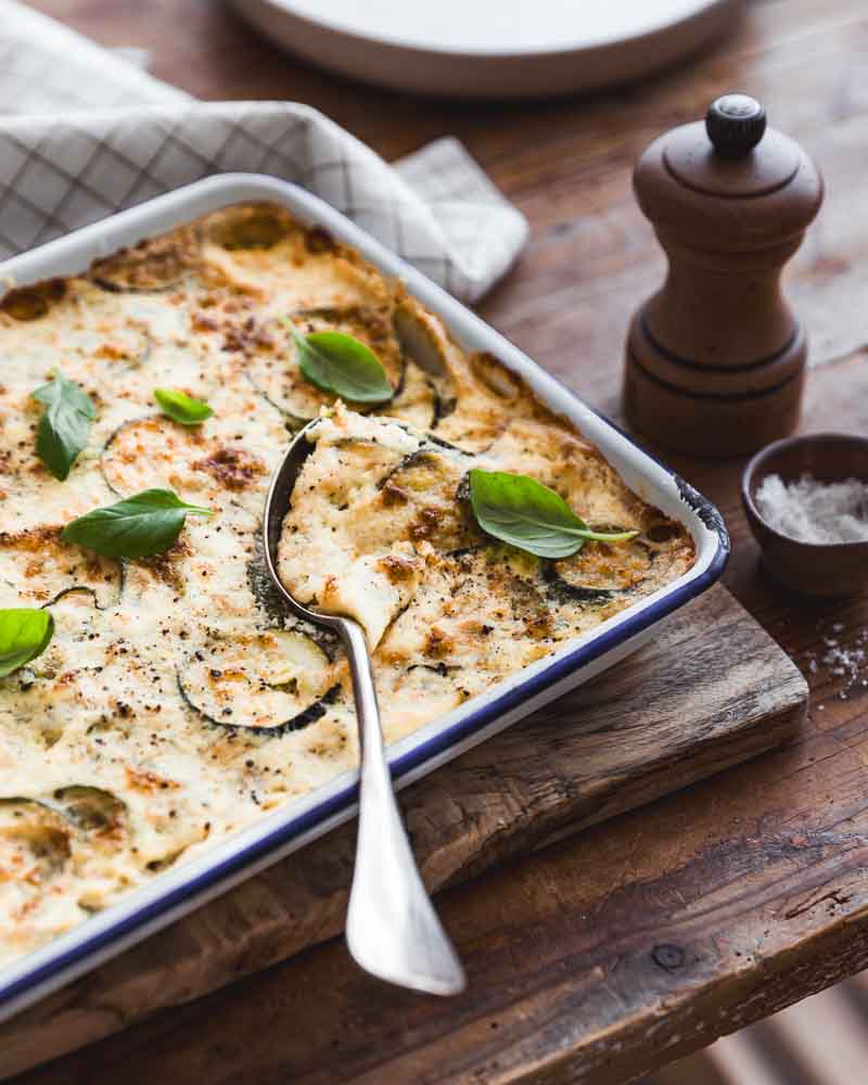 Gratin de courgettes végétal au tofu soyeux et crème de soja avec un peu de fromage de brebis posé sur une planche en bois dans une ambiance rustique