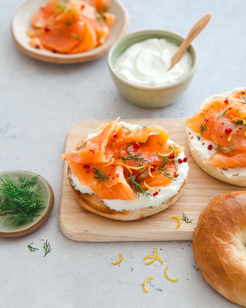 Bagel au saumon gravlax maison posés sur une planche en bois dans une ambiance assez minimaliste