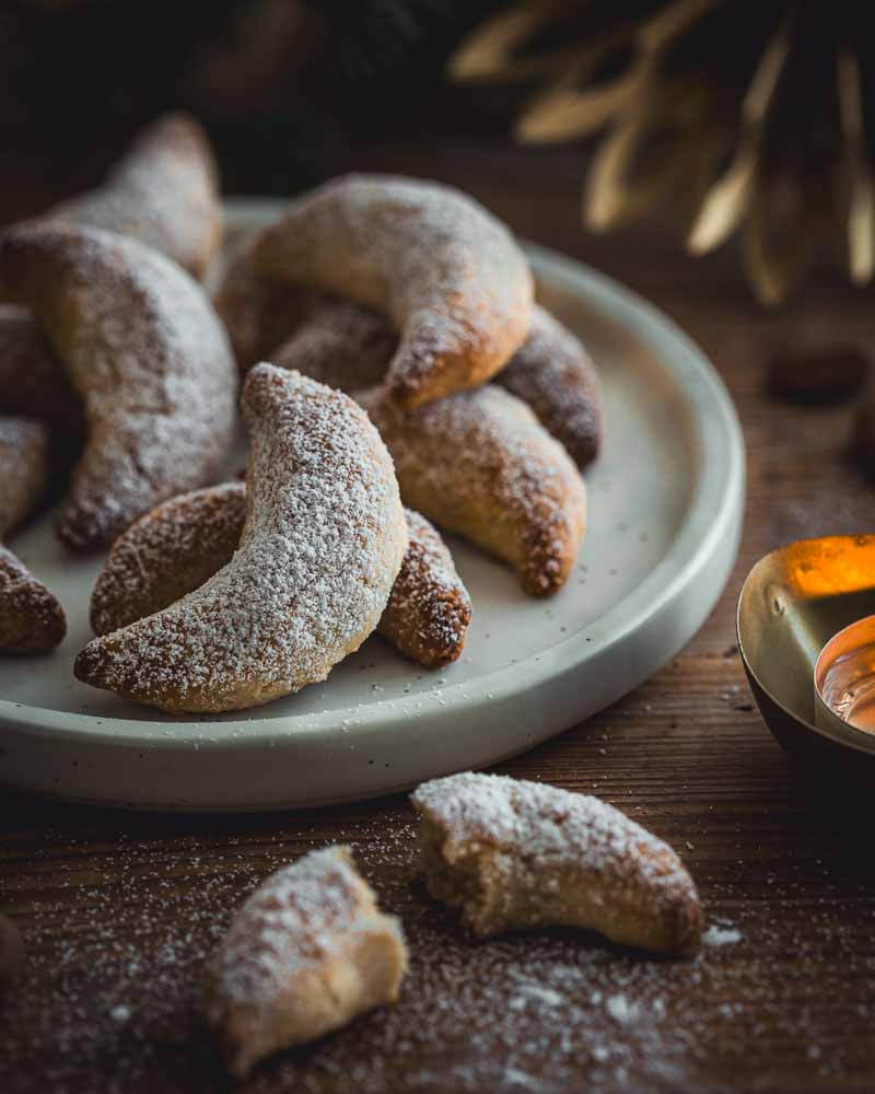 Gros plan sur une assiette de biscuits de noël aux amandes sans gluten comme des Vanille Kipferln. Ambiance chaleureuse de fin de journée sur table en bois. 