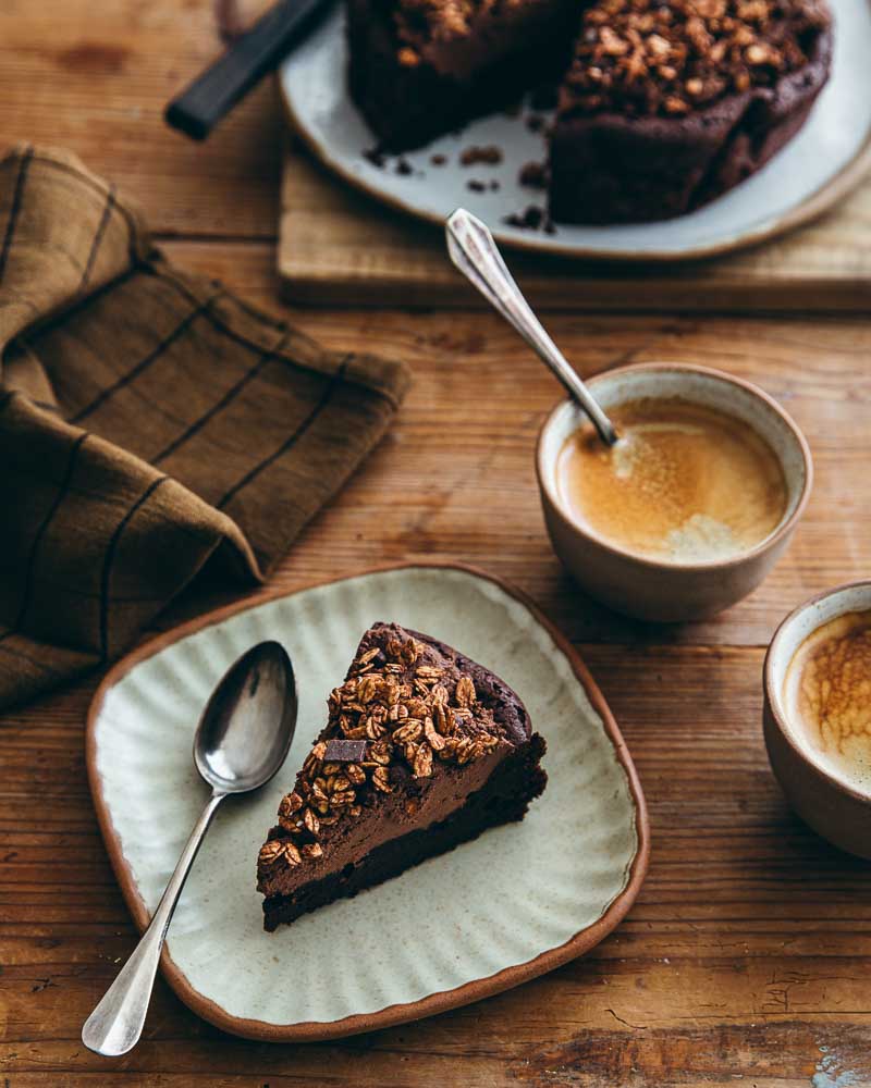Part de gâteau au chocolat sans gluten dans une assiette en céramique. A côté, deux tasses de café. 